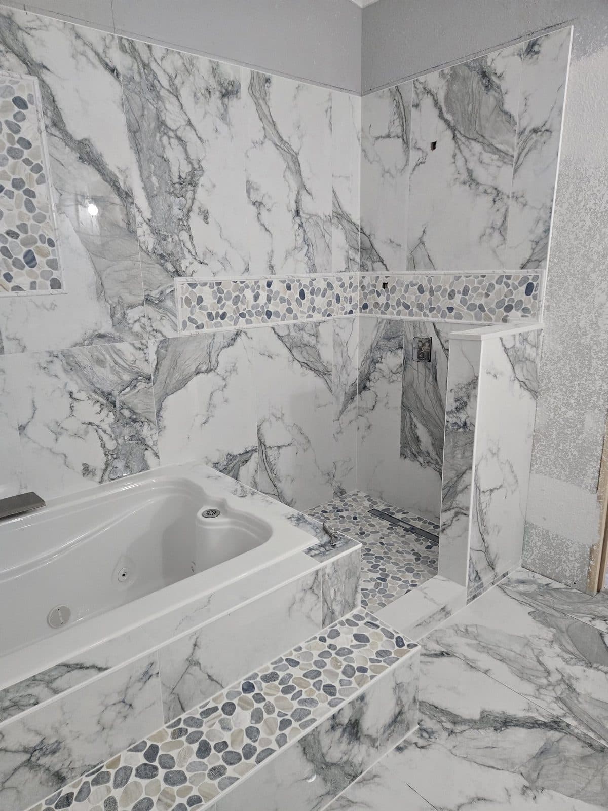 Corner jacuzzi and framed shower to marble-look porcelain with pebble accents — After